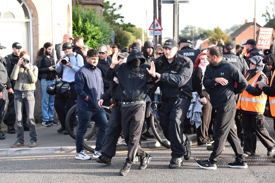 Police remove a protester who refused to remove their face mask outside the Merseyside Refugee Centre in Liverpool