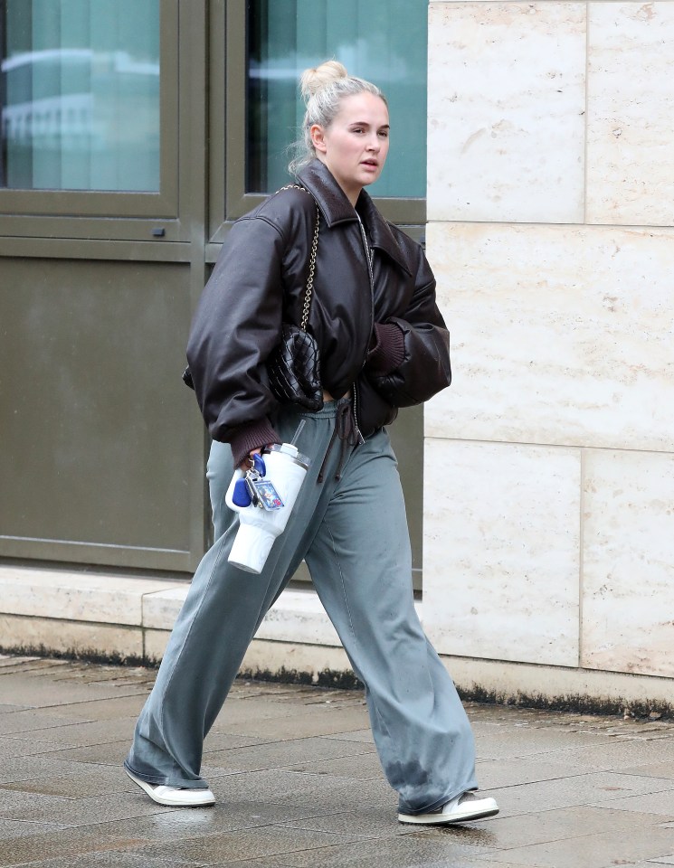 a woman wearing a brown jacket and grey pants is walking down the street