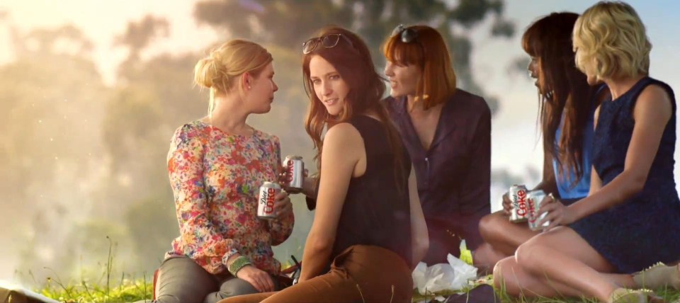 a group of women sitting on the grass holding cans of diet coke