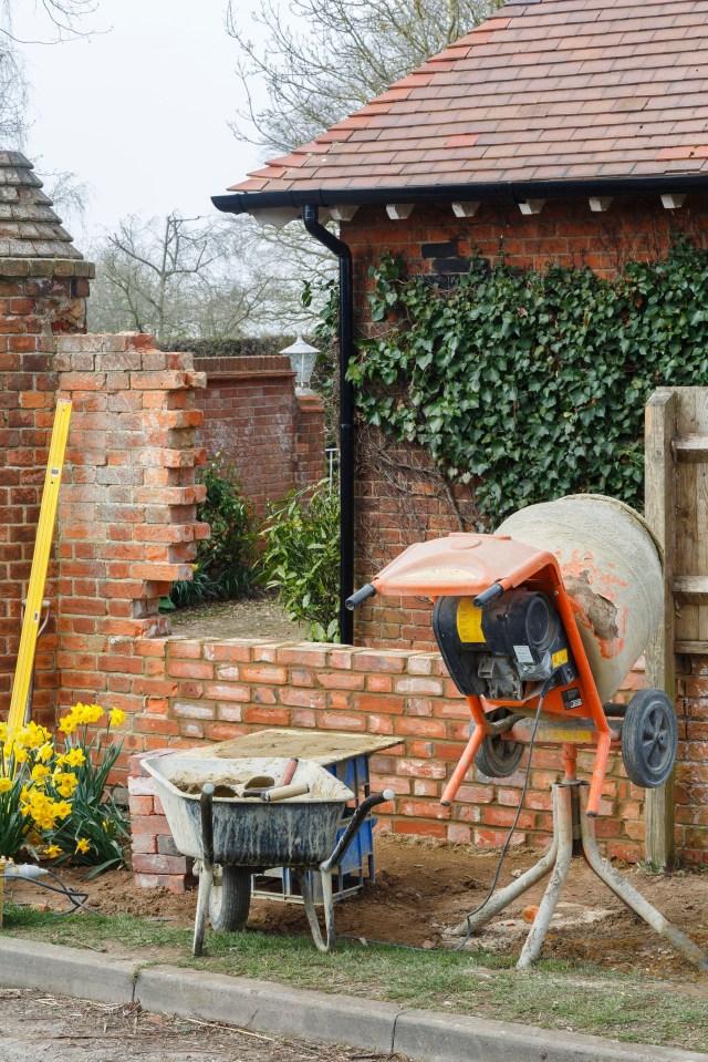 a brick wall is being built next to a wheelbarrow and a concrete mixer