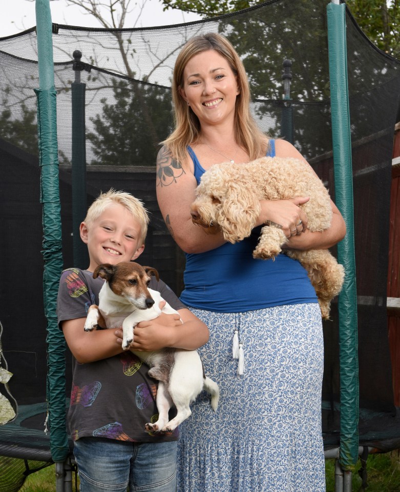 a woman and a boy holding two dogs in front of a trampoline