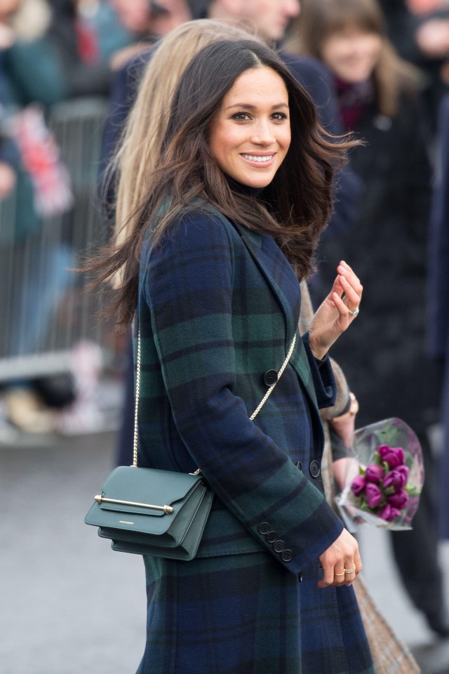 a woman in a plaid coat is smiling and holding flowers