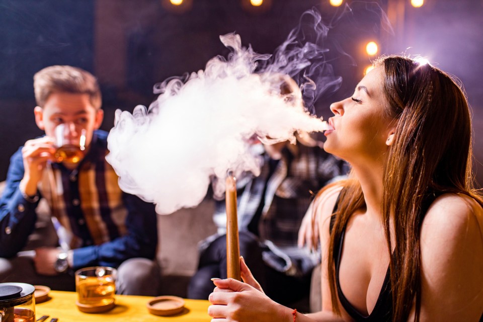 a woman is blowing smoke from a hookah while a man drinks from a glass