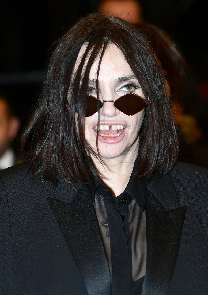 a woman wearing sunglasses and a tuxedo shows off her teeth