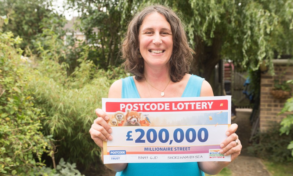 a woman holds up a postcode lottery ticket