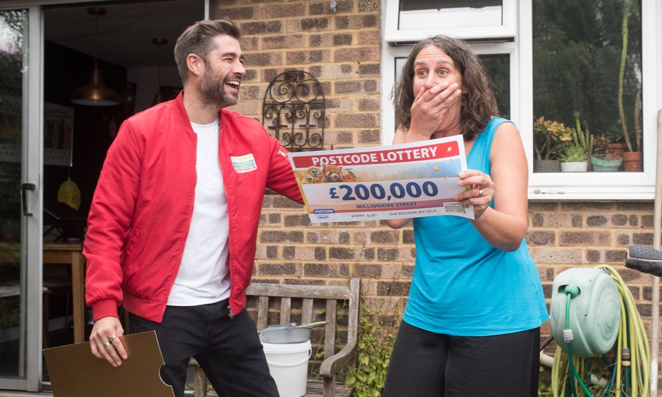 a woman is holding a postcode lottery ticket