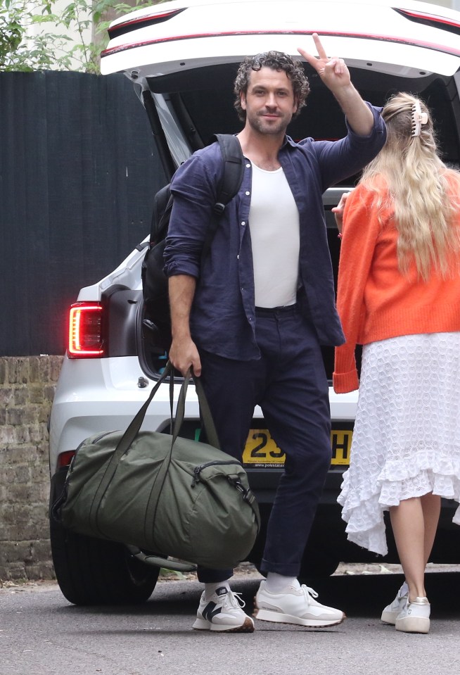 a man giving a peace sign in front of a car with a license plate that says 2jh