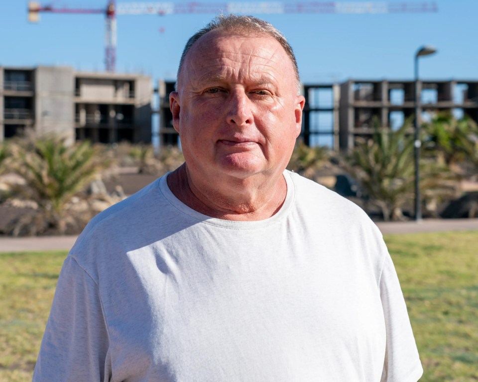 a man in a white shirt stands in front of a construction site