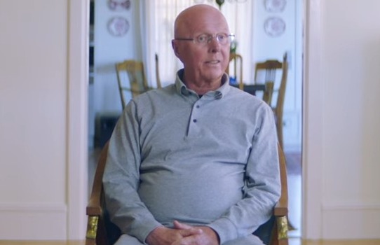 a man sits in a chair in a living room with a sign that says prime