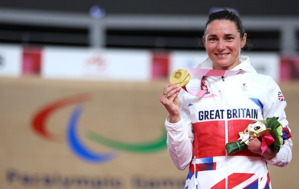 a woman in a great britain jacket holds up her gold medal