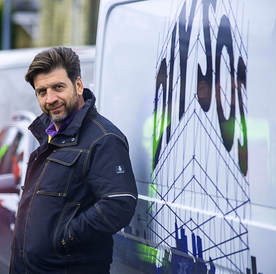 a man in a black jacket leans against a white van