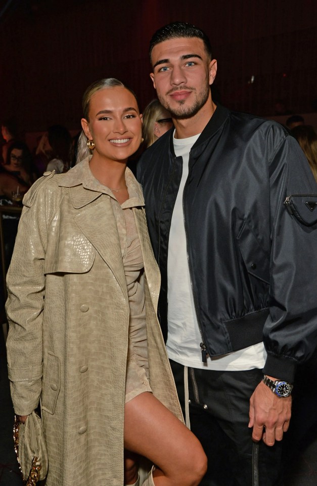 a man and a woman are posing for a picture and the woman is wearing a trench coat