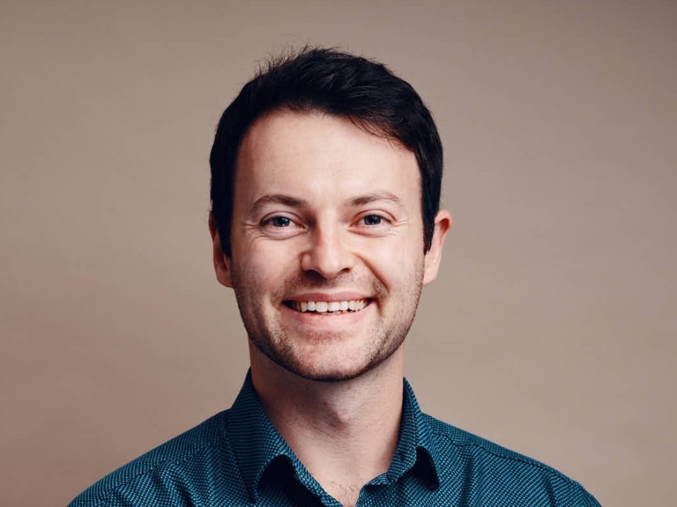 a man in a blue shirt smiles with his arms crossed