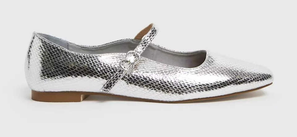 a pair of silver ballet flats with a strap around the ankle on a white background .