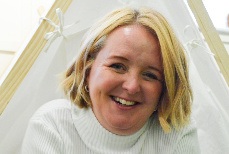 a woman in a white sweater smiles in front of a white tent