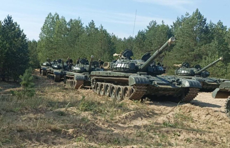 a row of military tanks are parked on a dirt road