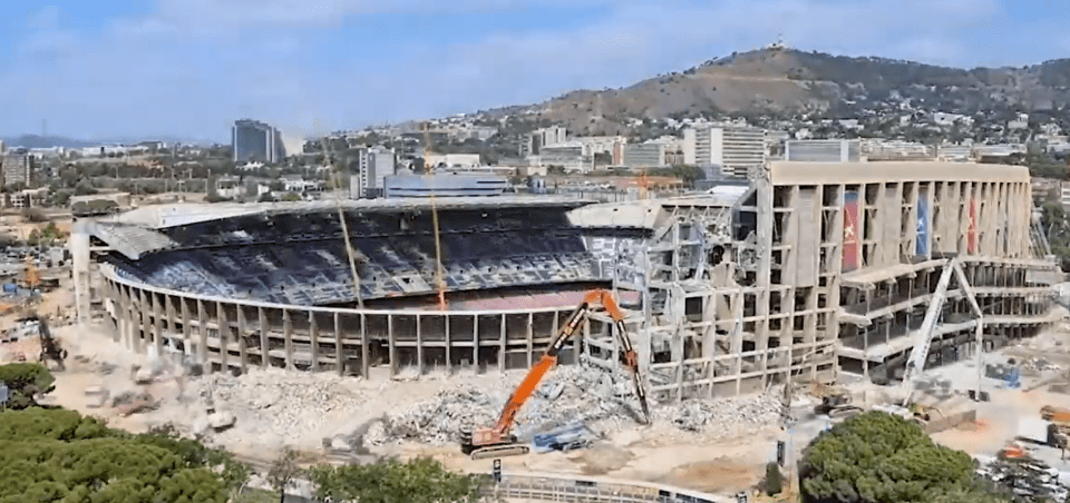 a large stadium is being demolished with a large orange excavator in the foreground