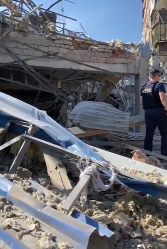 a man in a press vest stands in front of a pile of rubble