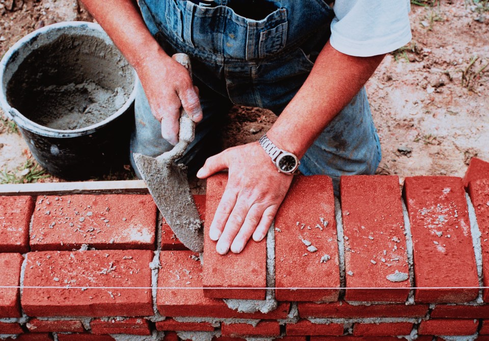 a man wearing a watch is working on a brick wall