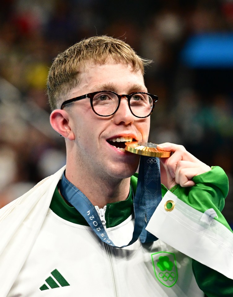 a man wearing glasses is biting into a gold medal from the olympics