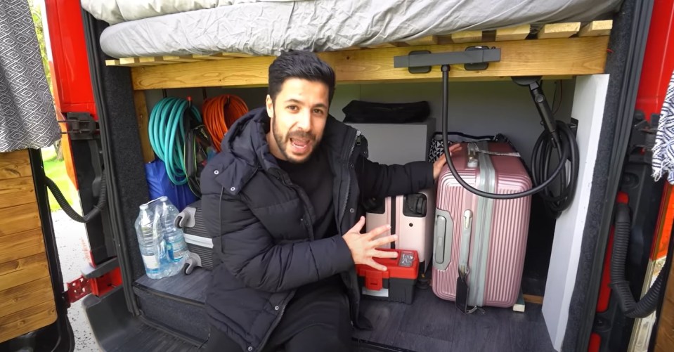 a man sitting in the back of a van holding a pink suitcase