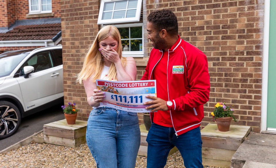 a woman is holding a postcode lottery ticket