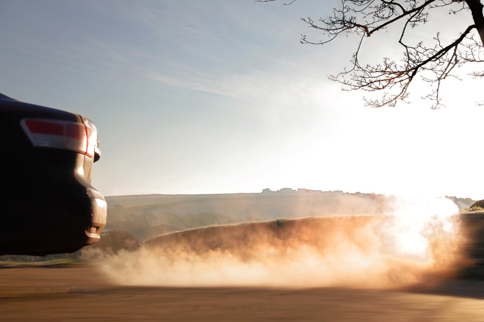 a car is driving down a dirt road with smoke coming out of it