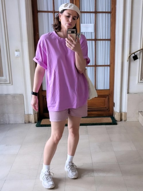 a woman in a purple shirt and shorts is taking a selfie