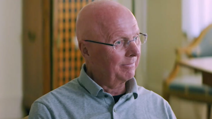 a bald man wearing glasses and a grey shirt