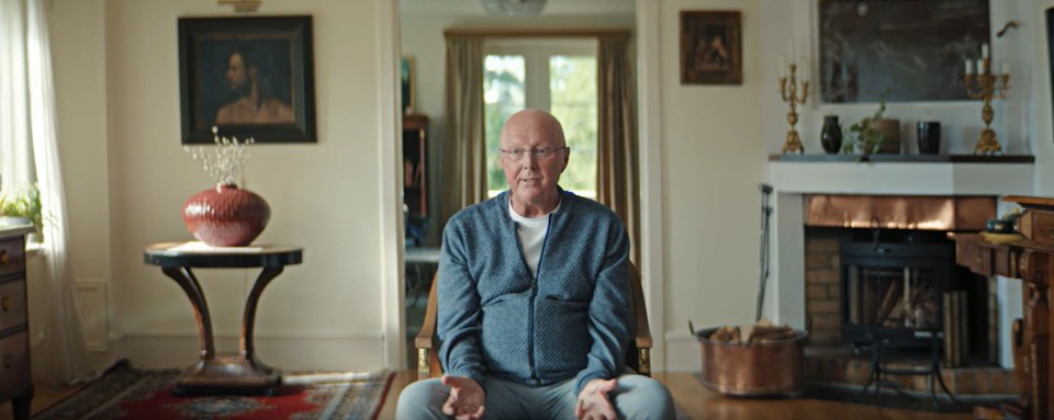 an elderly man sits in a chair in a living room