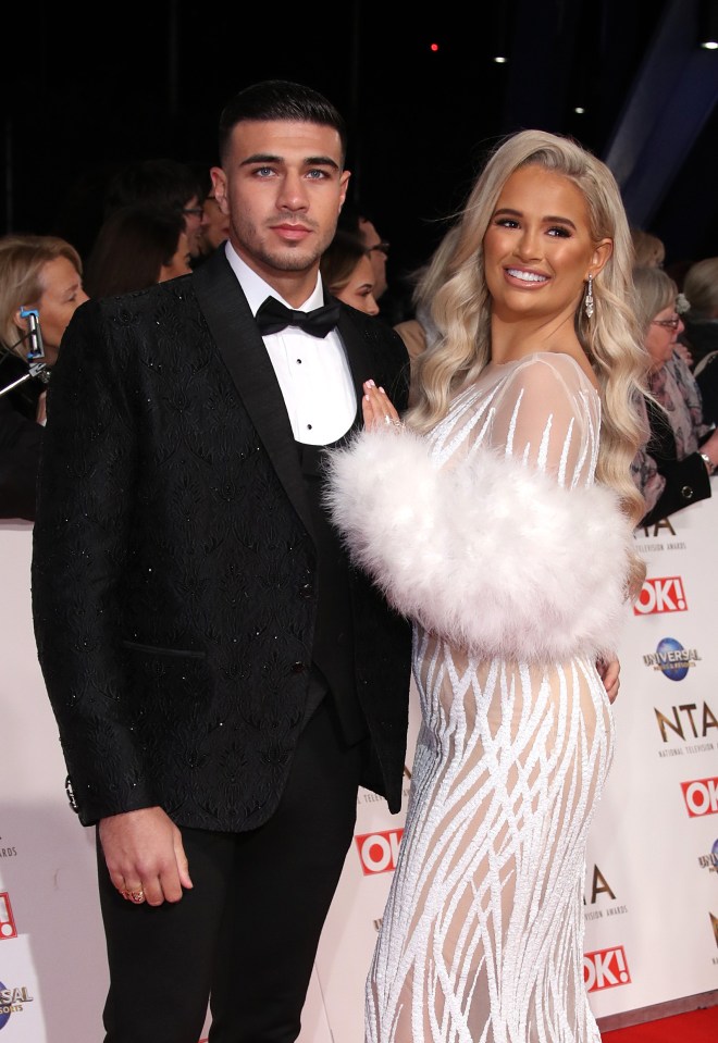 a man in a tuxedo and a woman in a white dress pose on the red carpet