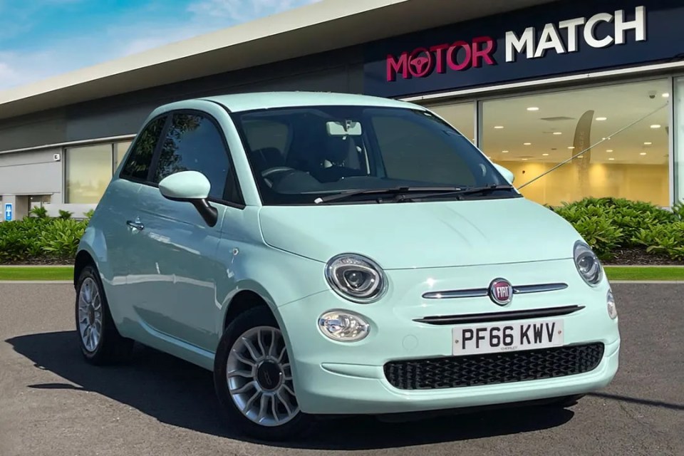 a light blue fiat car is parked in front of a motor match dealership