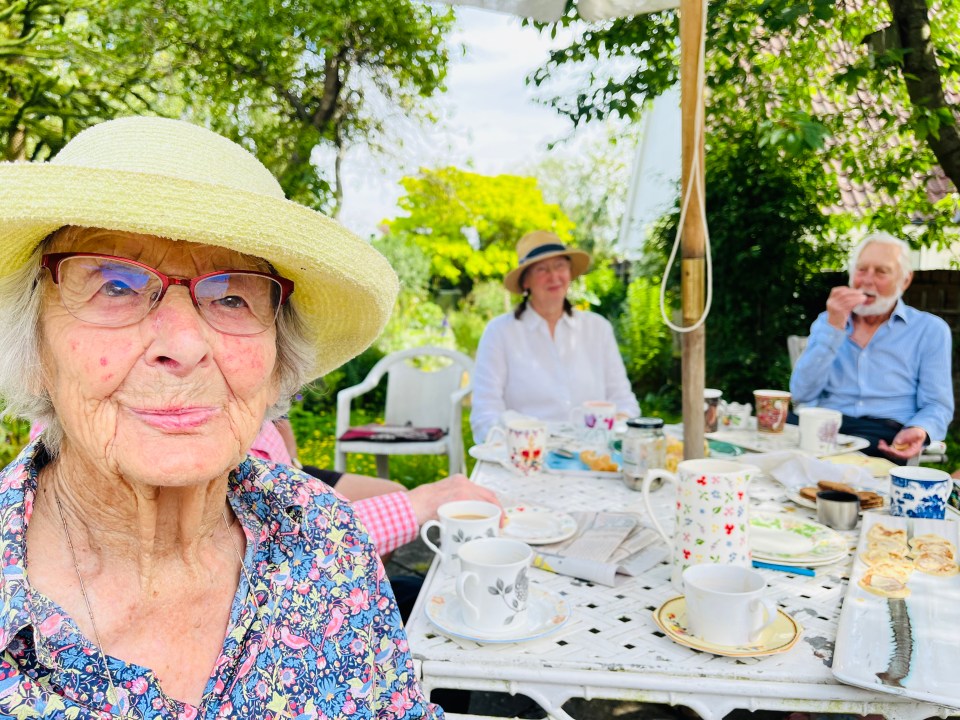 an elderly woman wearing a hat sits at a table with other people