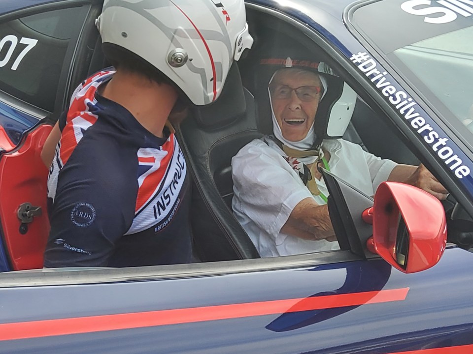 a man wearing a helmet sits in a car with a #drivesilverstone sticker on the windshield