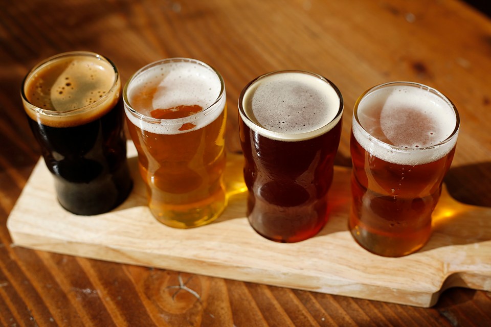 four glasses of beer are lined up on a wooden cutting board