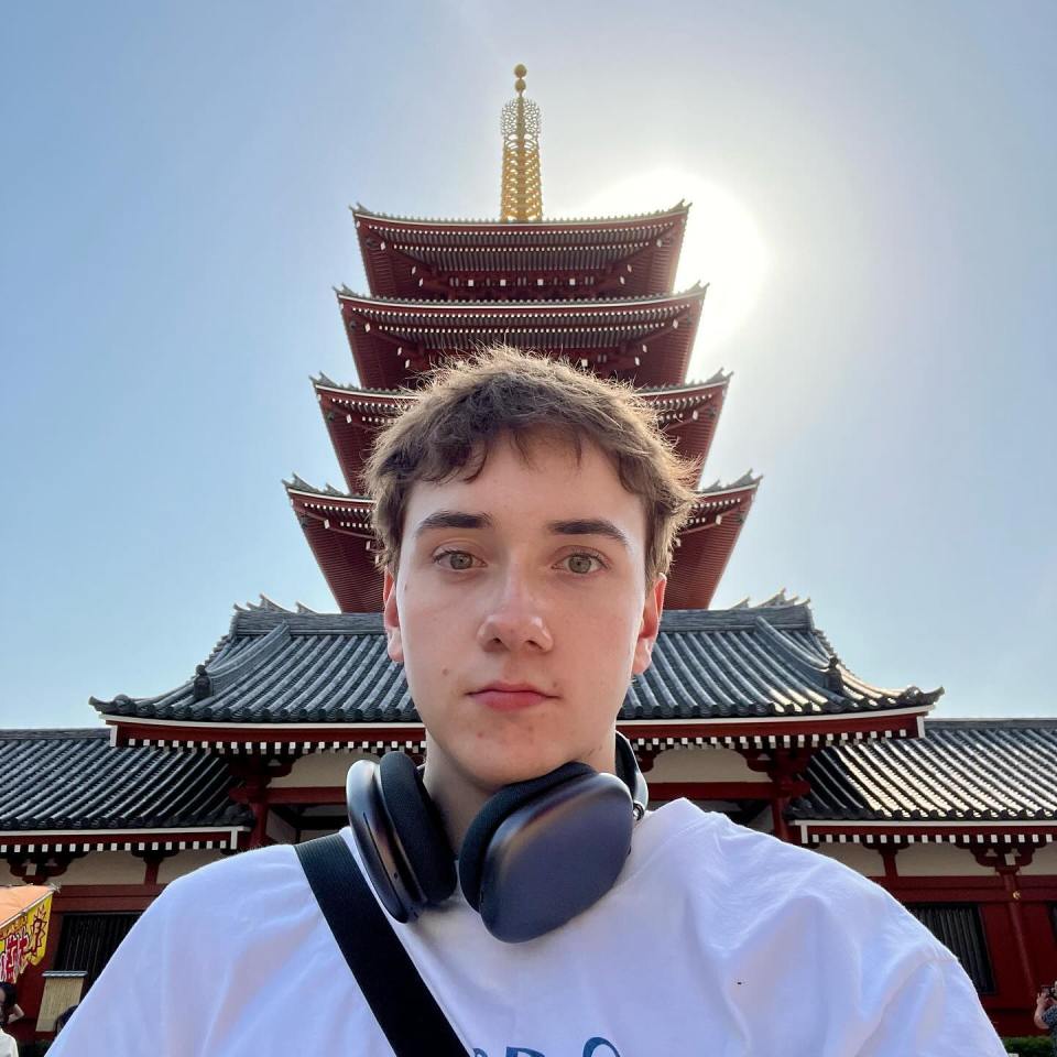 a man wearing headphones stands in front of a pagoda