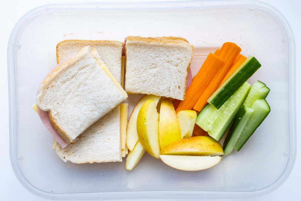 a plastic container filled with sandwiches apples carrots and cucumbers