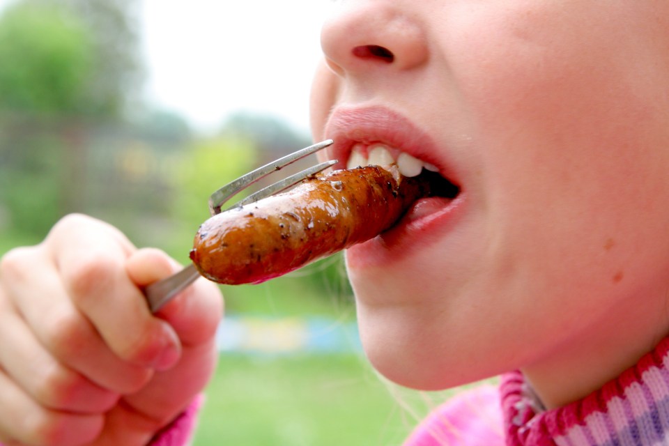 a young girl is eating a sausage with a fork