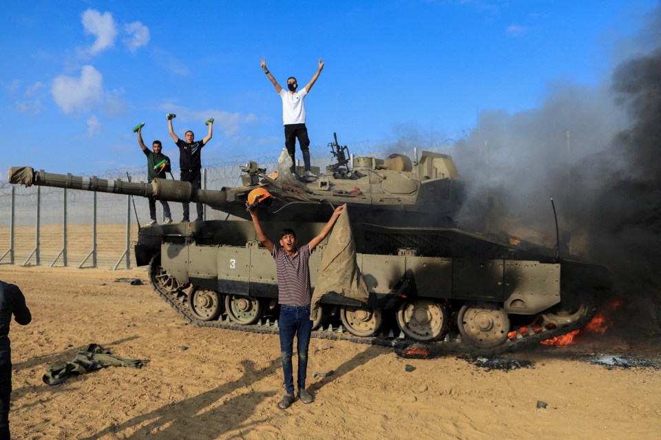 Palestinians celebrate as an Israeli military vehicle burns after it was hit by Palestinian gunmen who infiltrated areas of southern Israel, at the Israeli side of Israel-Gaza border, October 7, 2023. REUTERS/Yasser Qudih NO RESALES. NO ARCHIVES. TPX IMAGES OF THE DAY