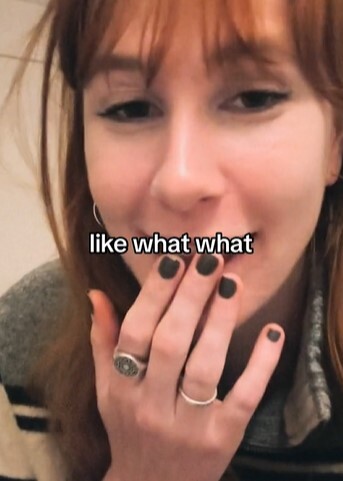 a woman with black nails and a ring on her finger is covering her mouth with her hand .