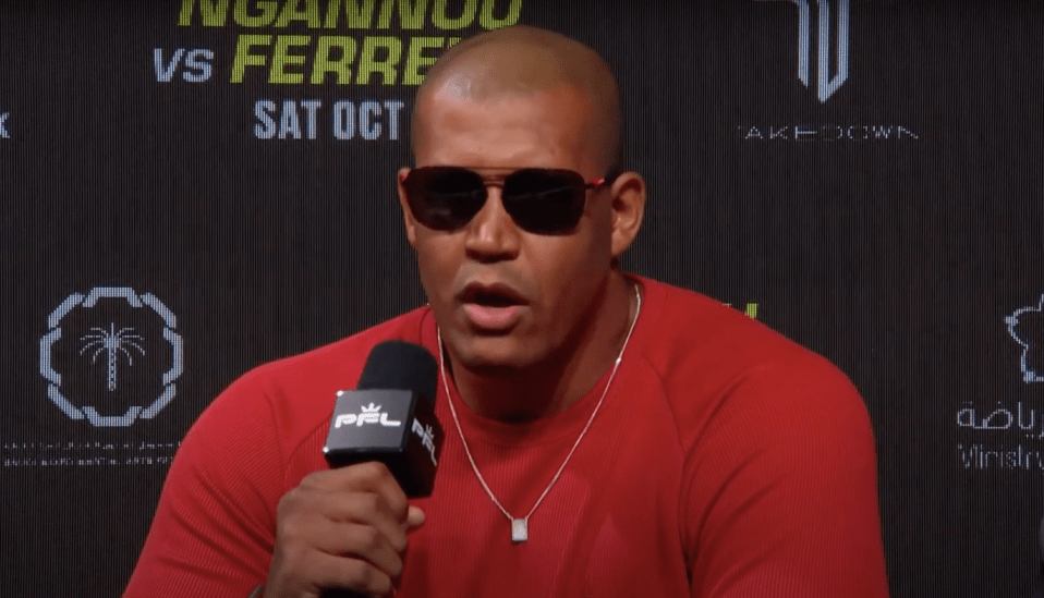 a man wearing sunglasses and a red shirt is speaking into a ppl microphone