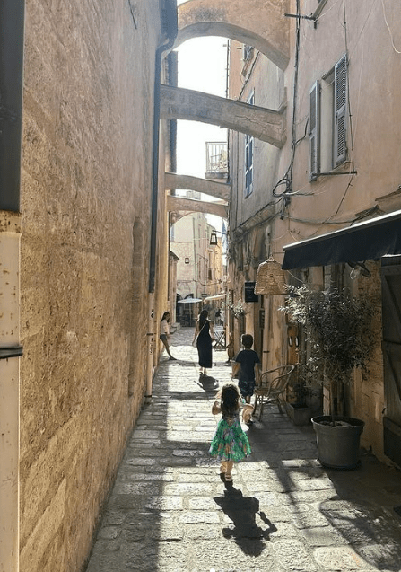 a little girl in a dress is walking down a narrow street