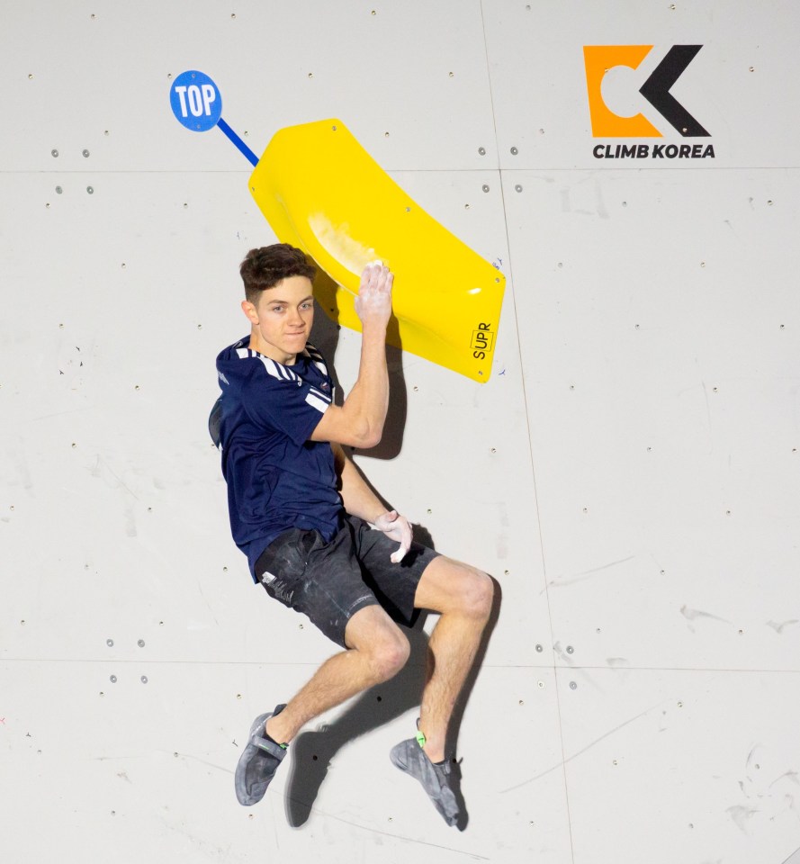 a man is climbing a wall with a climb korea logo in the background