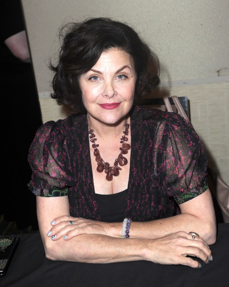 a woman wearing a necklace and a bracelet sits with her hands folded