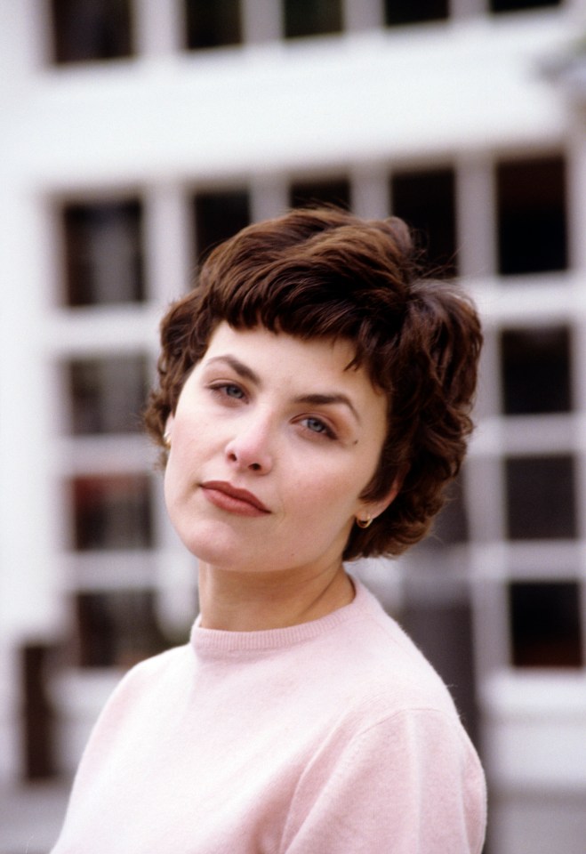 a woman in a pink sweater looks at the camera