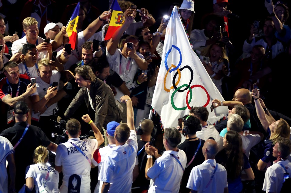 a man in a france shirt holds up the olympic flag