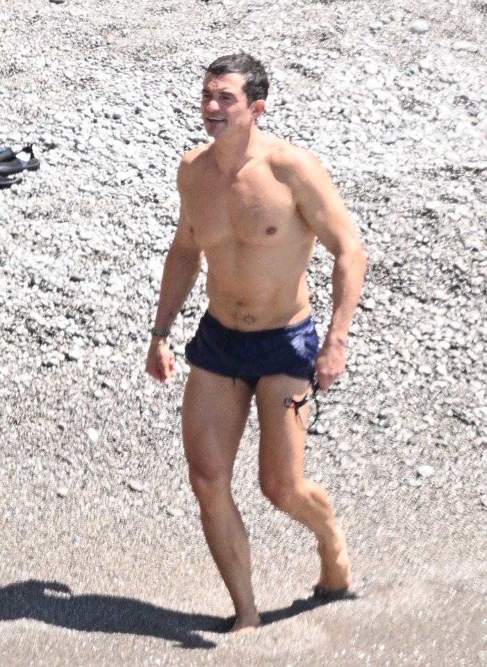 a shirtless man in blue shorts is walking on a rocky beach