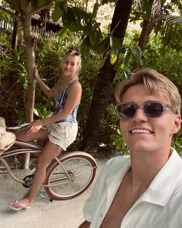 a woman sitting on a bike next to a man wearing sunglasses