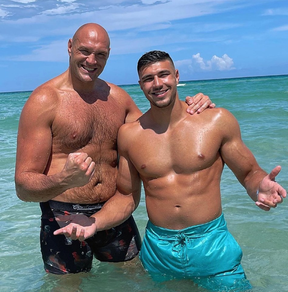 two men are posing for a picture in the water and one of them is wearing a pair of budweiser shorts