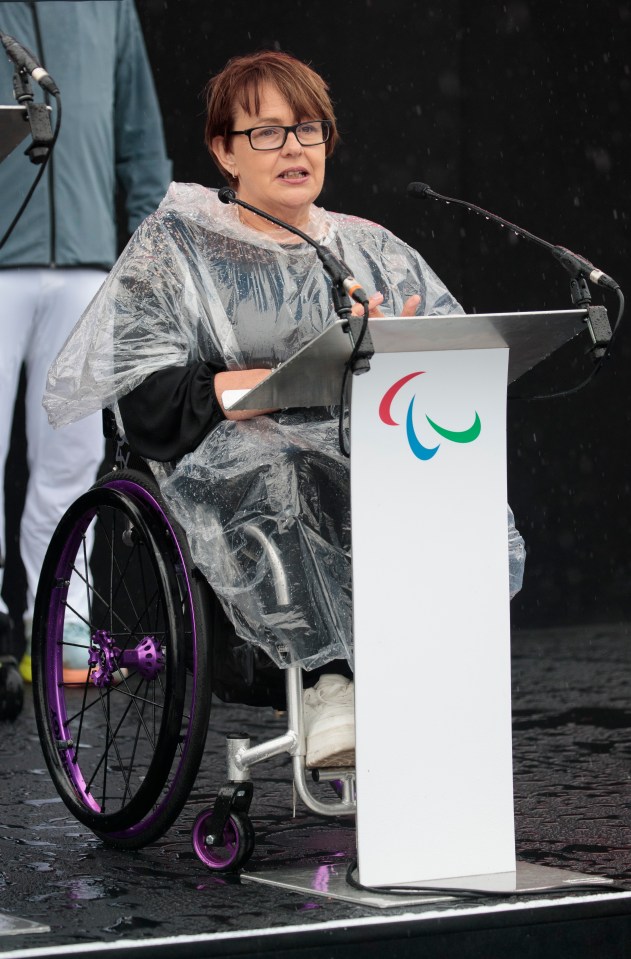 a woman in a wheelchair stands at a podium with a paralympic logo on it